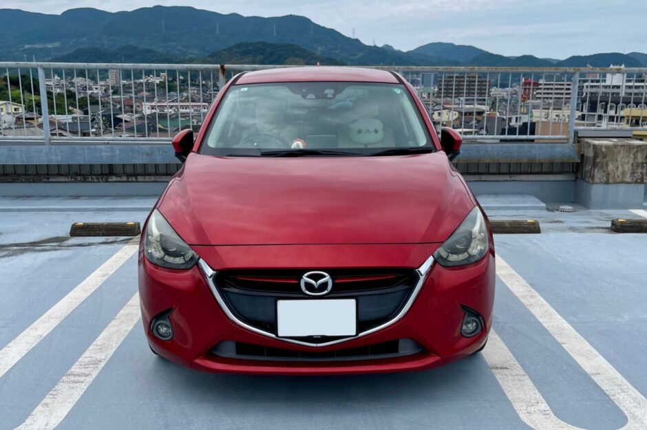 屋上駐車場に停めた赤いマツダ・デミオの正面