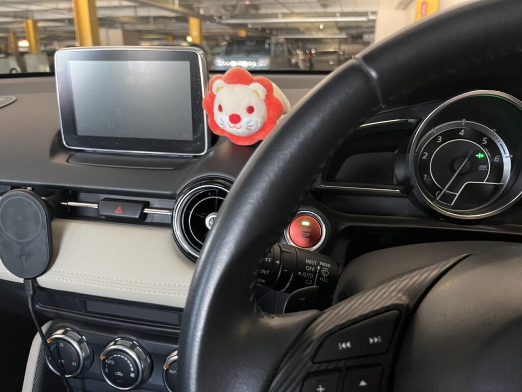車のハンドルとダッシュボード、赤いお守りのストラップが下がっている様子
